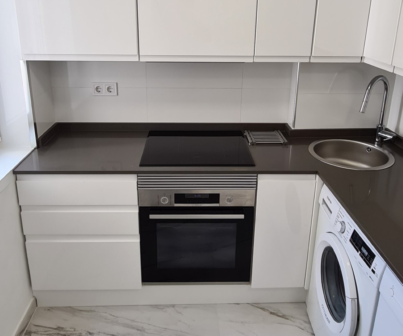 Cocina reformada con muebles blancos, horno y placa de inducción